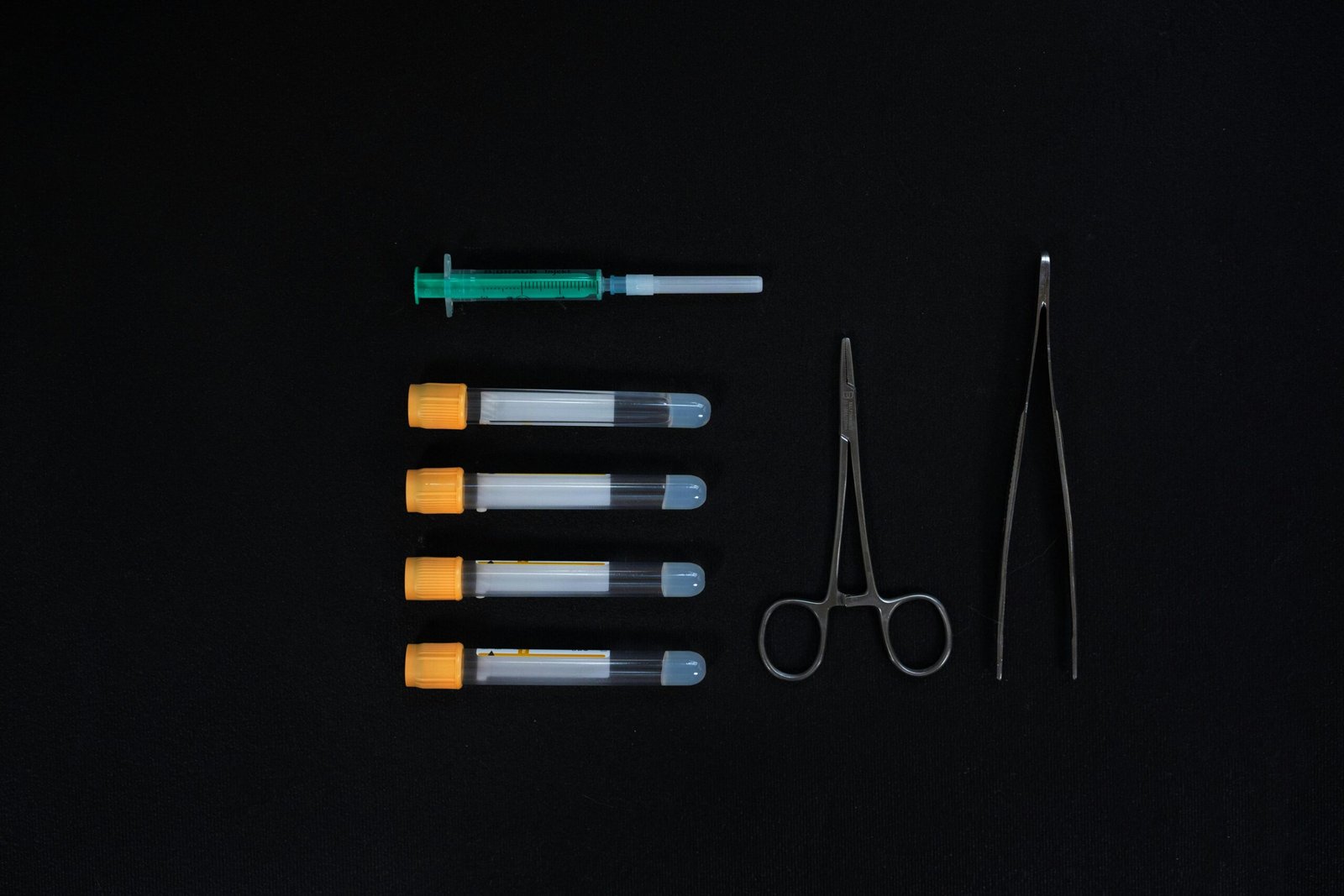 Top view of medical tools including syringes and test tubes on a black background.
